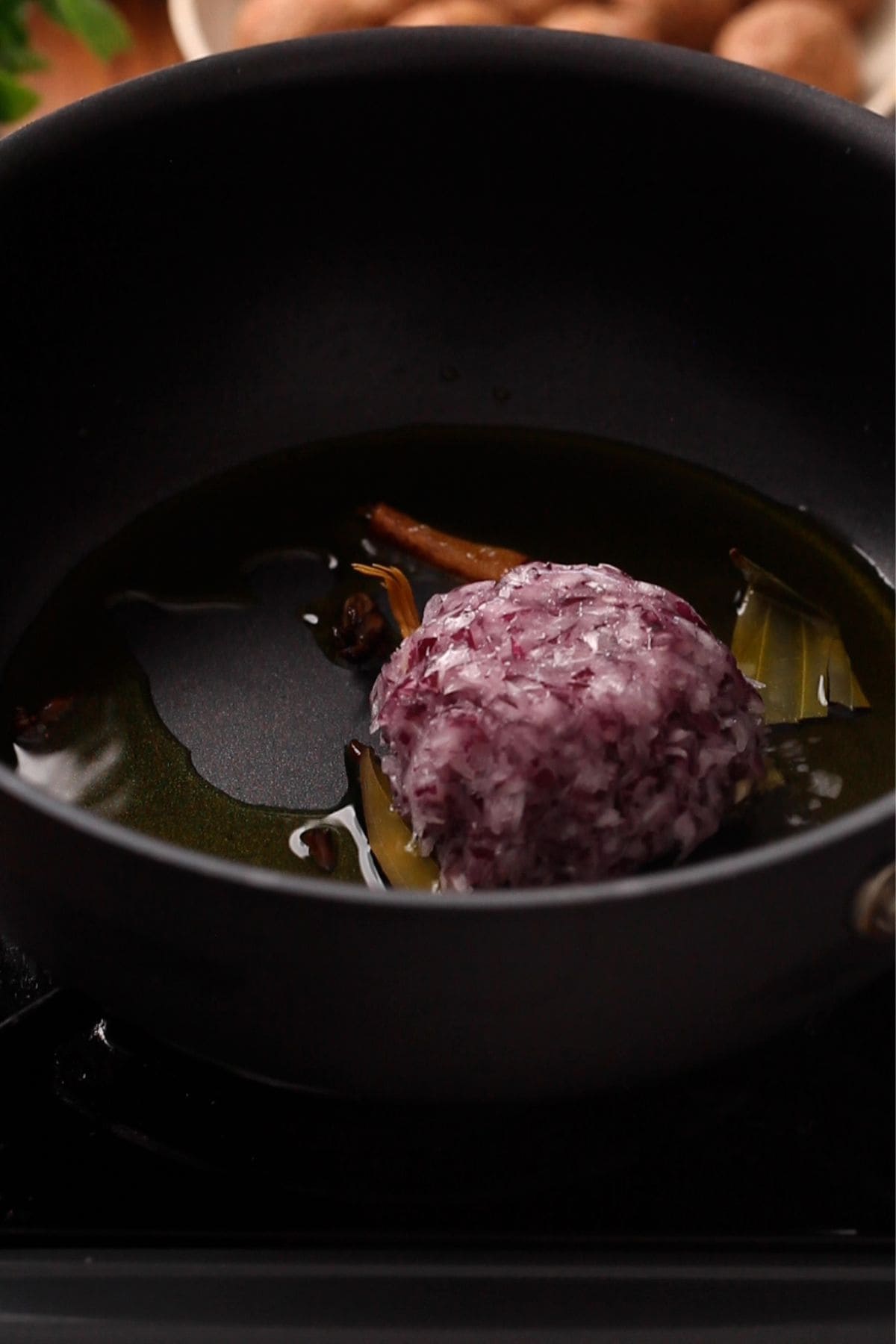 Whole spices and onions in oil in a black cooking pot.