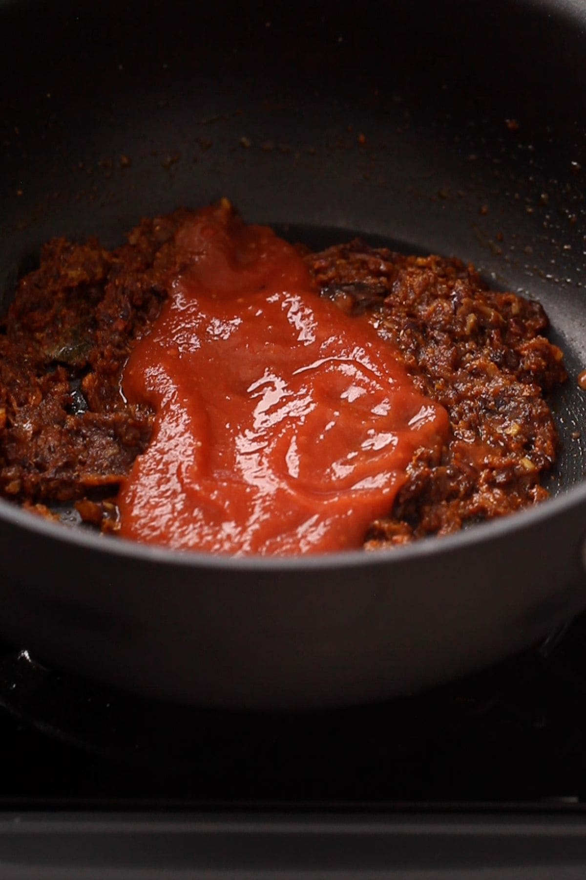 Tomato puree is added to the onion and spices.