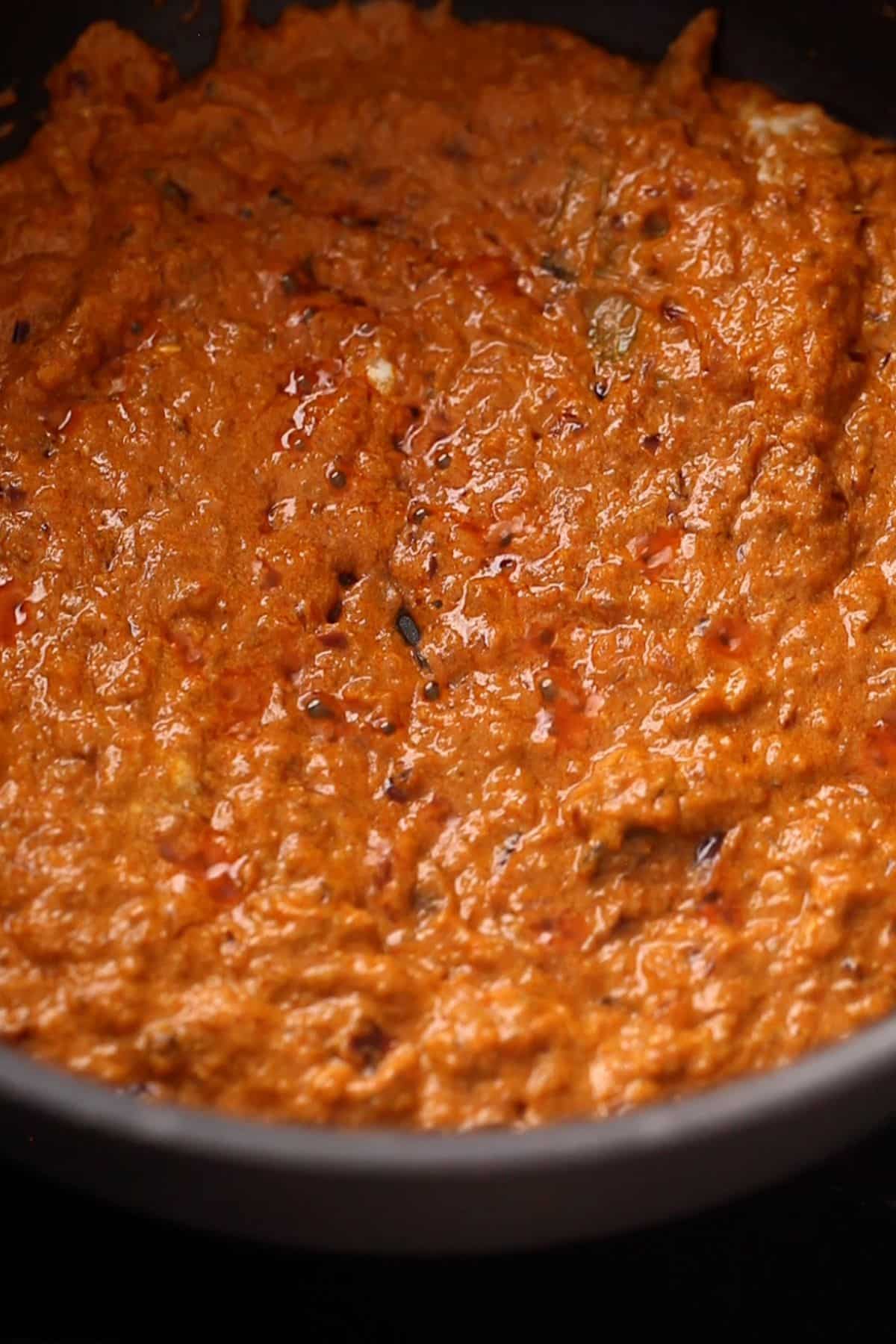 A close-up of a thick, reddish-brown masala paste. with visible oil on the surface and a textured, chunky appearance.