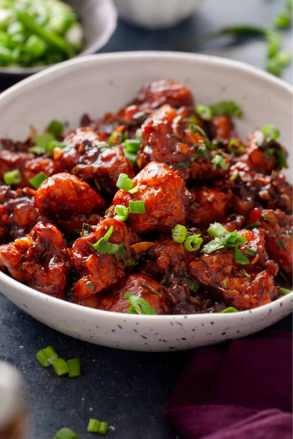 Side View of cauliflower manchurian with green onions in background.