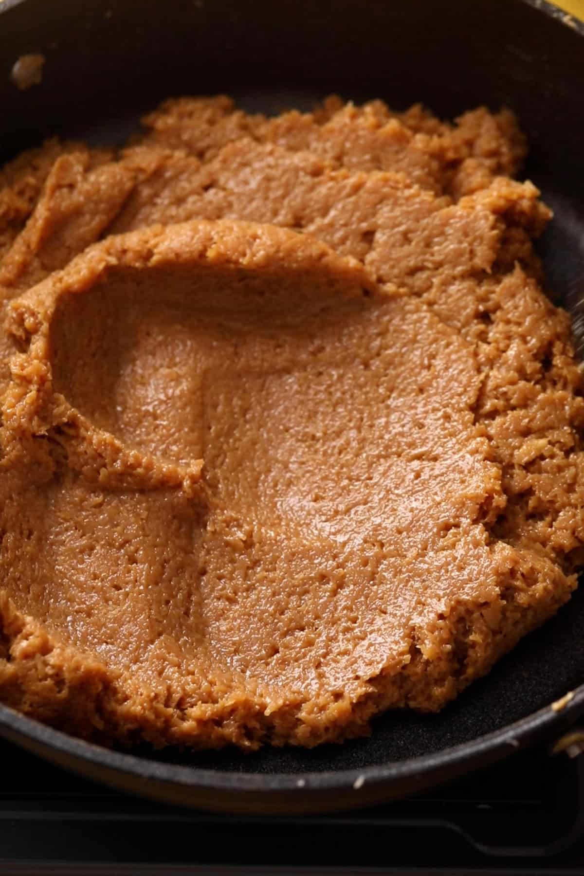 Smoother looking coconut barfi mixture in black pan.