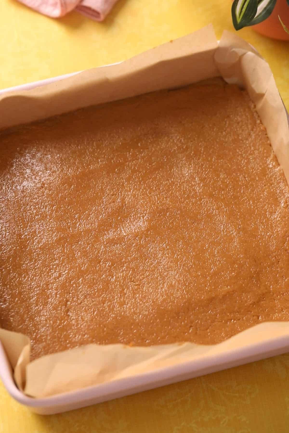 Coconut burfi mixture is added to a 8 by 8 parchment tray.