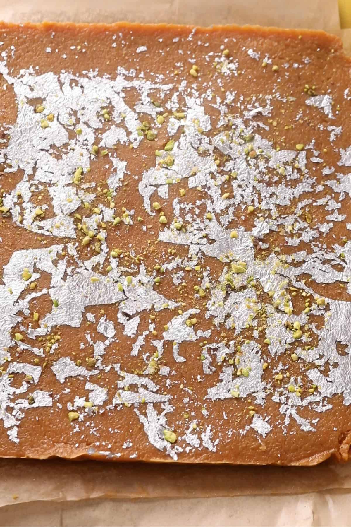 Edible silver foil and chopped pistachios are added to the set coconut burfi.