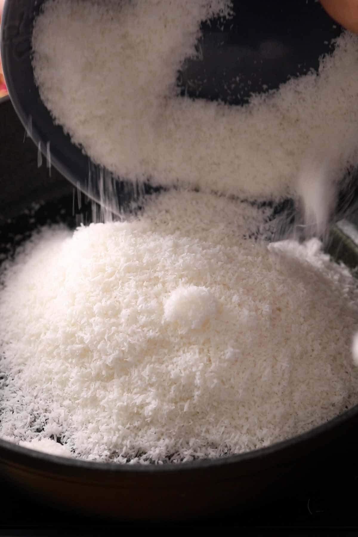 Dessicated coconut is added to melted ghee in a black pan.