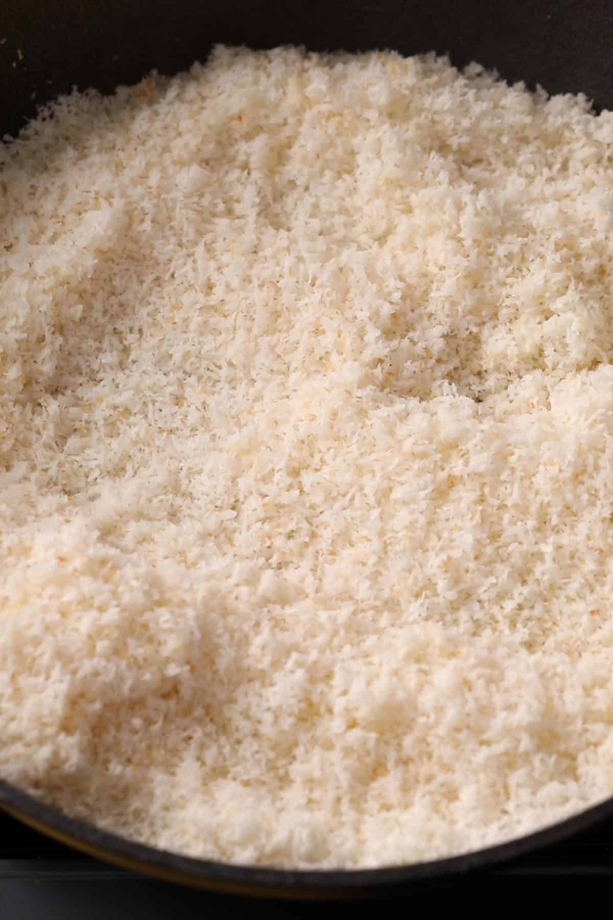 Lightly toasted coconut in ghee in a black pan.