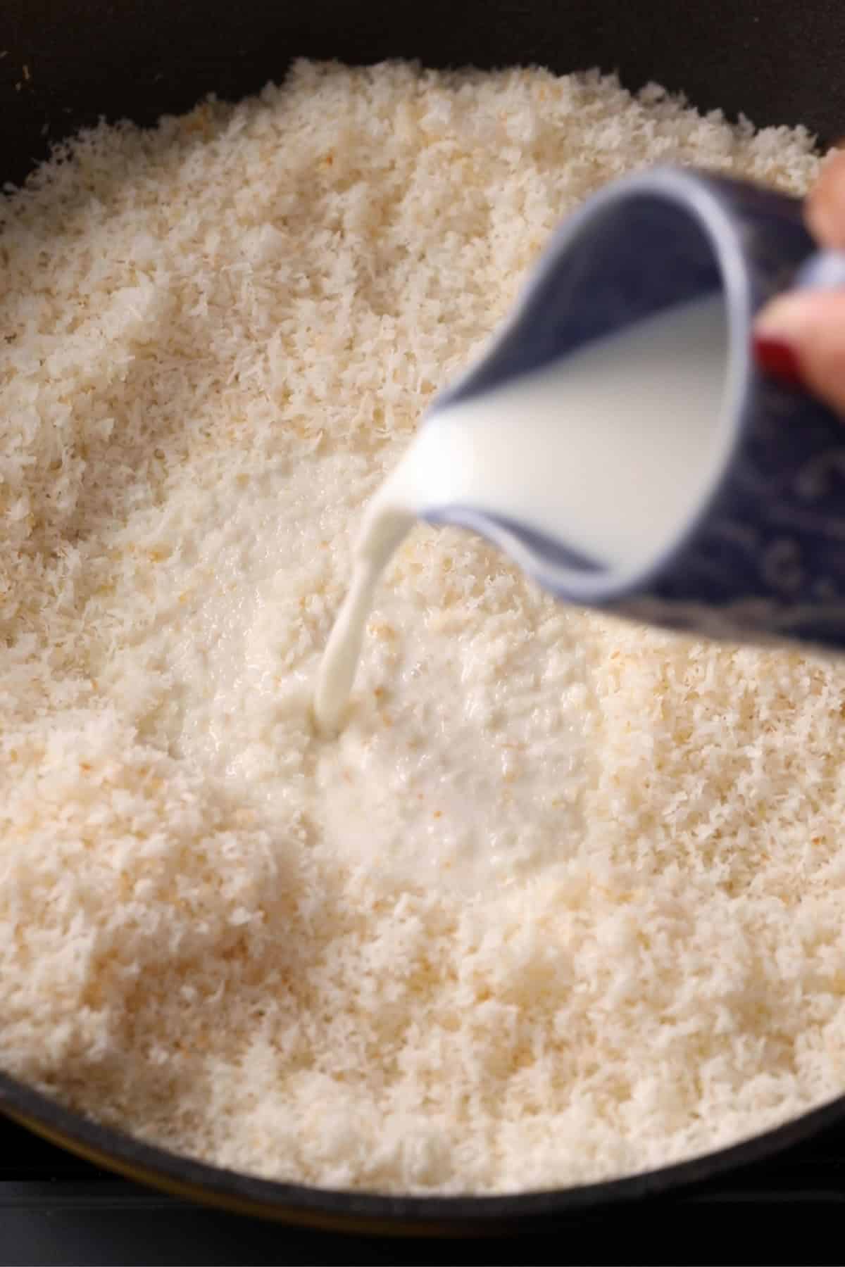 Milk is poured using a blue cup intp the toasted coconut.