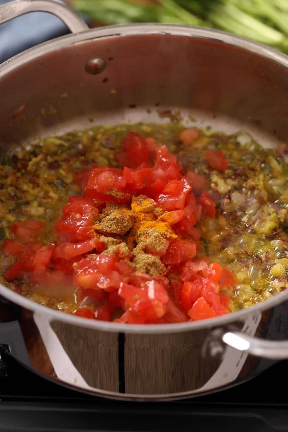 Chopped tomatoes and spices are added to a pan with sautéed onions , cooking together on a stovetop.