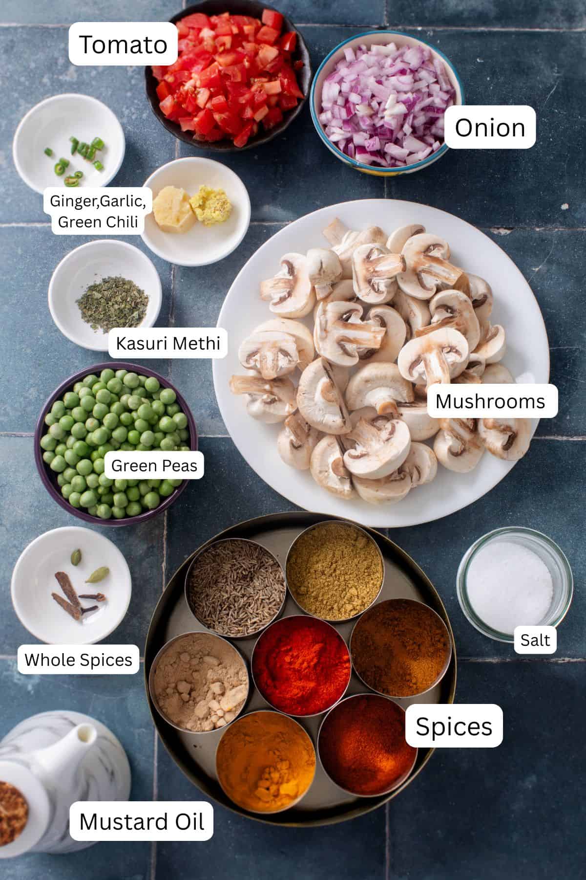 Ingredients needed to make Mushroom Matar Masala placed n a tiled dark background.