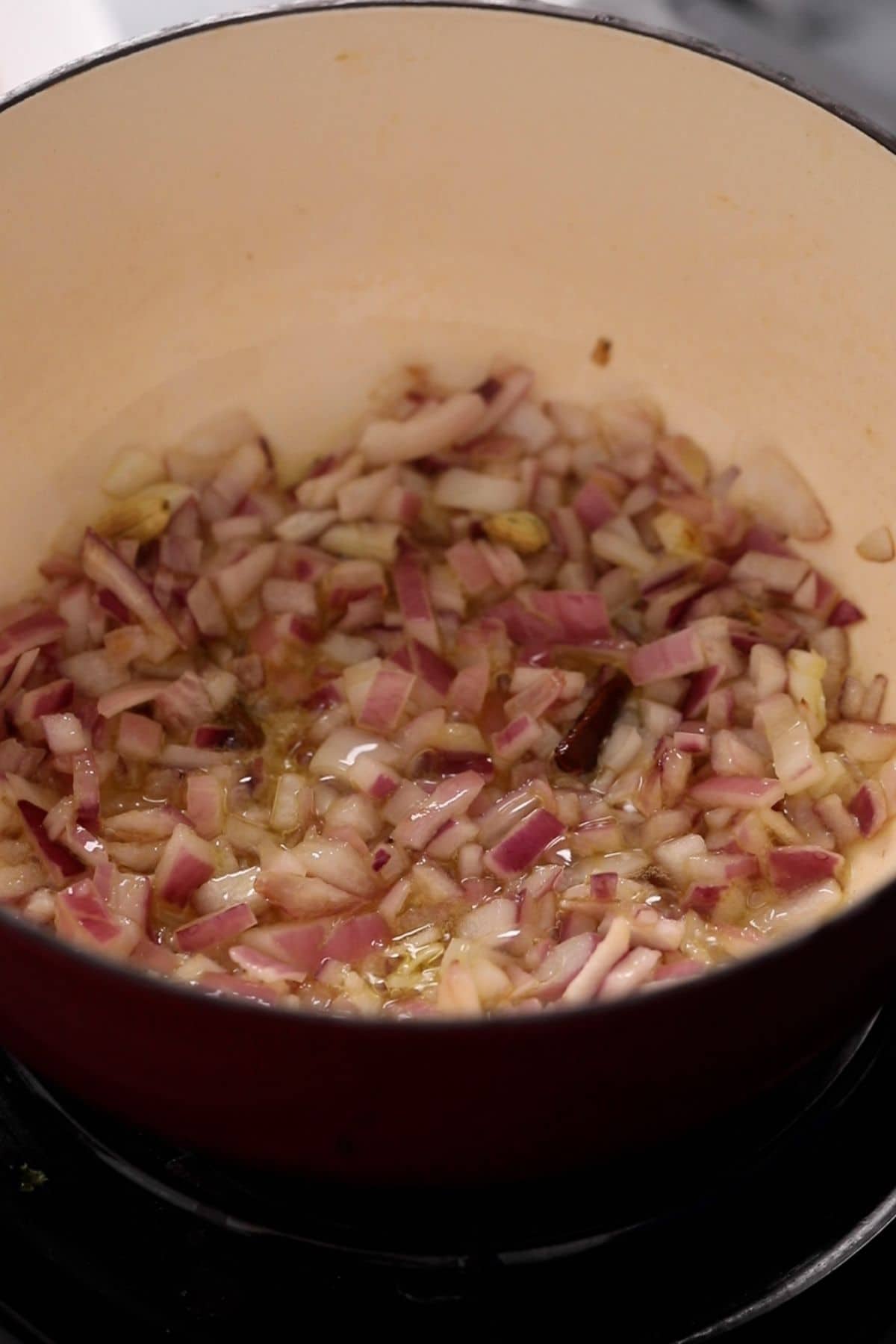 Whole spices and onions are browning in oil in an enameled cooking pot.