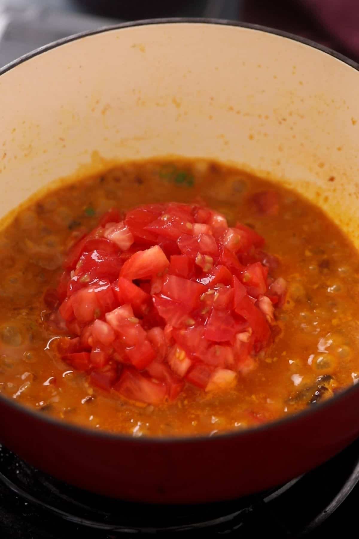 Chopped tomatoes are added to the masala in an enameled cooking pot.