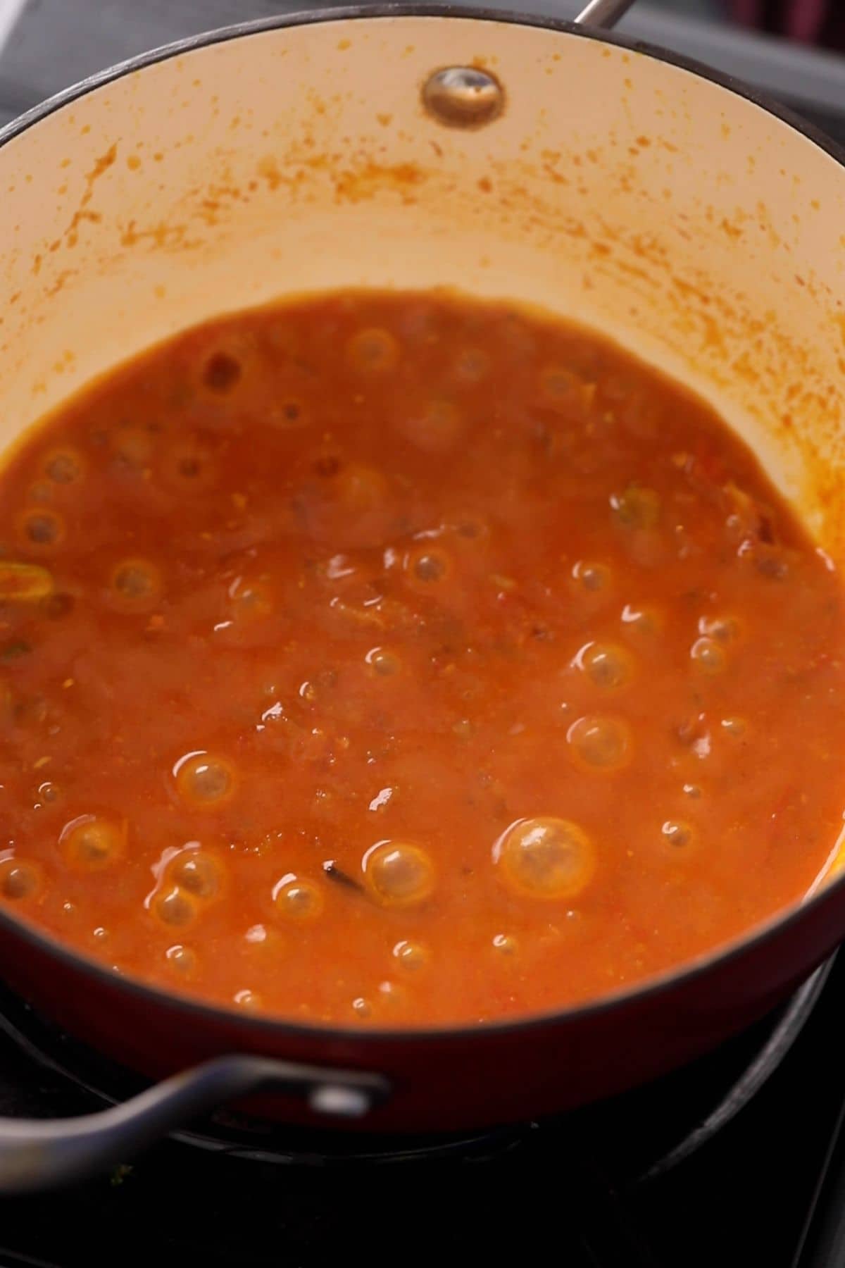 Tomatoes are cooking down and bubbling in the cooking pot for mushroom matar sabzi.