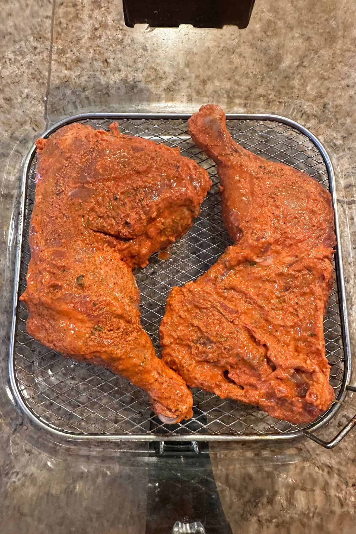 Marinated tandoori chicken placed on steel rack of a glass air fryer basket.