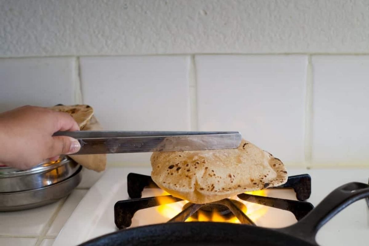 Roti is being cooked on open flame on stove.