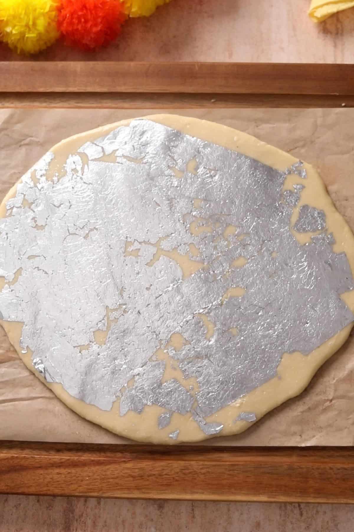 Edible silver foil is placed all over the rolled kaju katli dough.