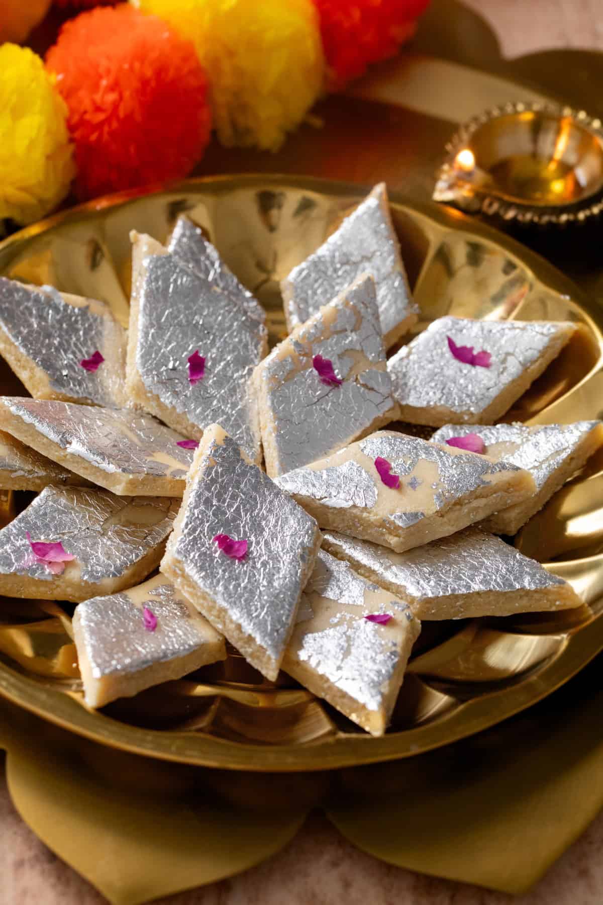Side view of kaju katli with a lit diya in background.