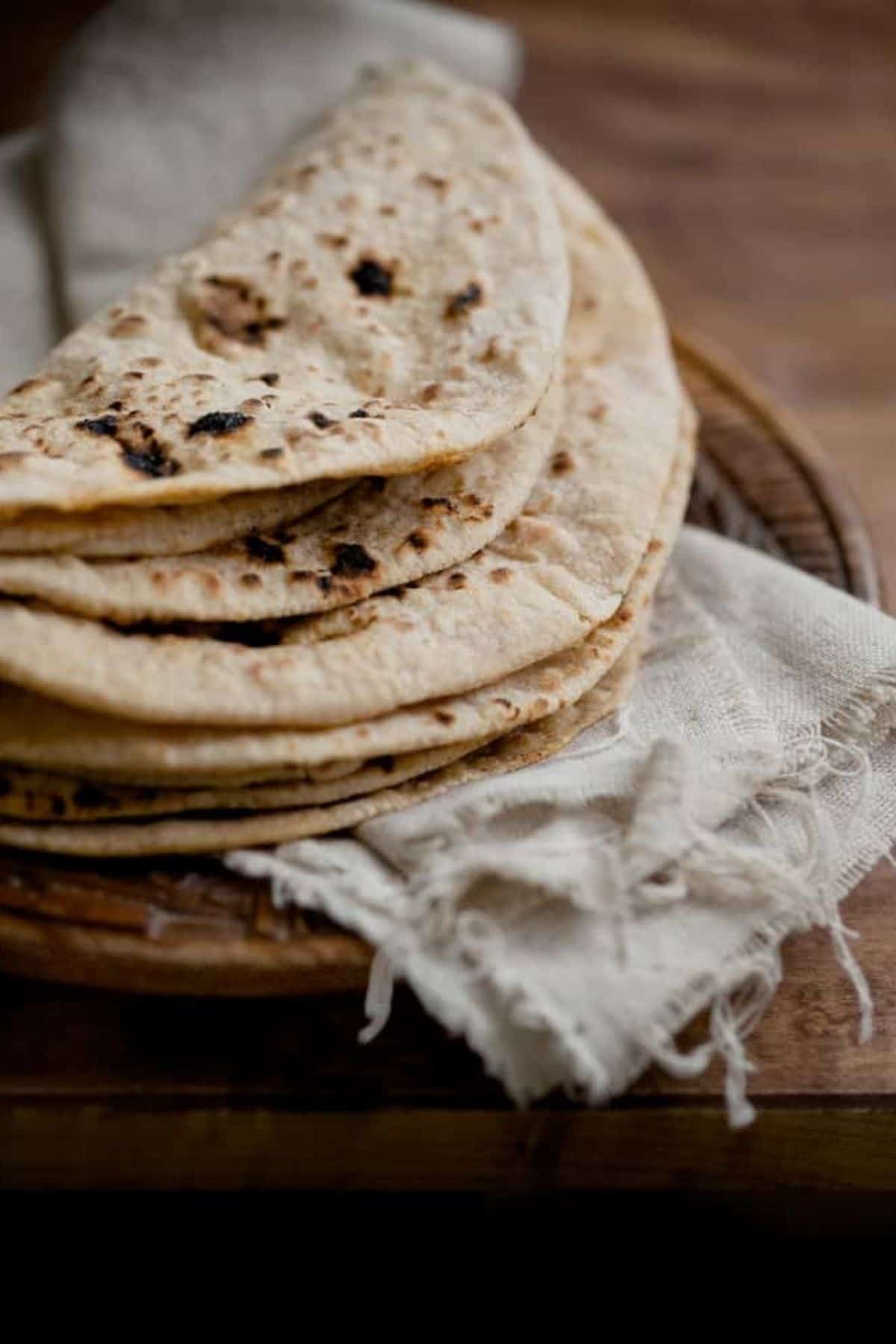 A bunch of rotis folded and kept on a linen on a wooden plate.