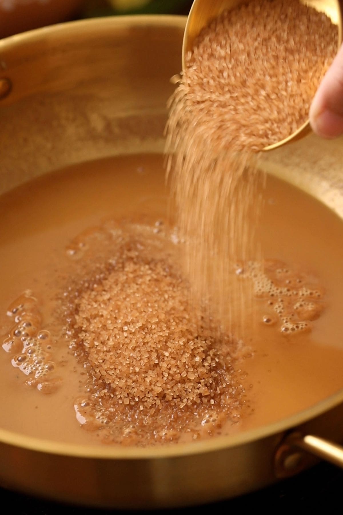 Raw sugar is being sprinkled on the ghee and flour mixture.
