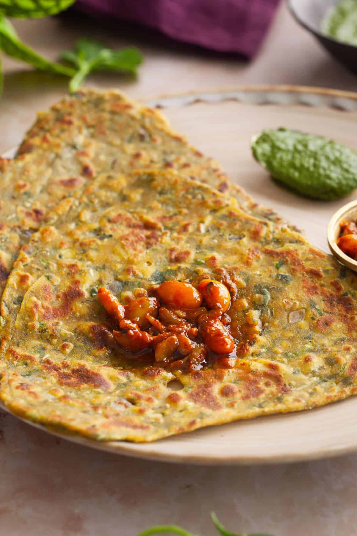 Side view of methi paratha with garlic pickle served on top of it.