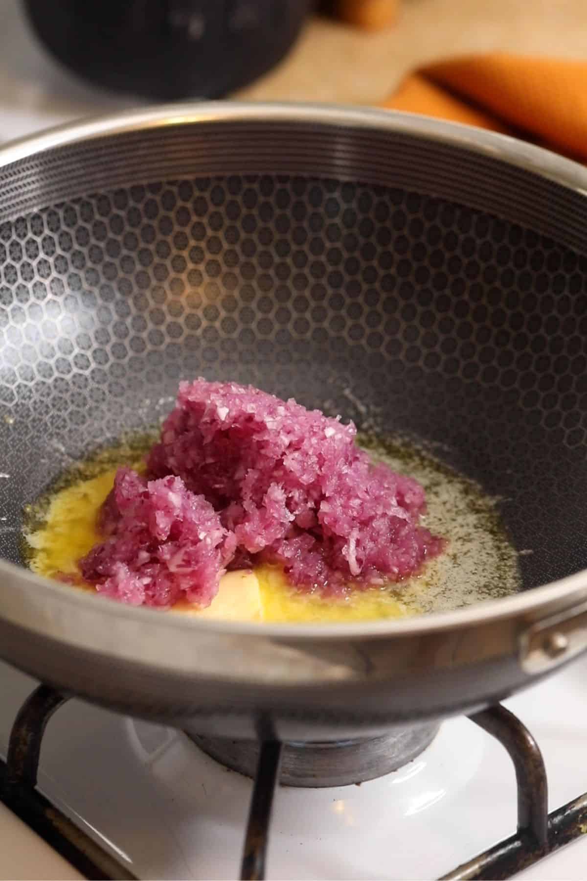 Finely chopped onions are added to butter in a black steel wok.
