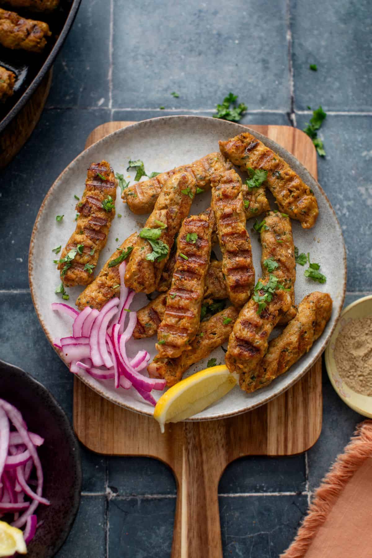 Chicken Seekh kebab served on a white plate with lemon wedge and onion slices. 
