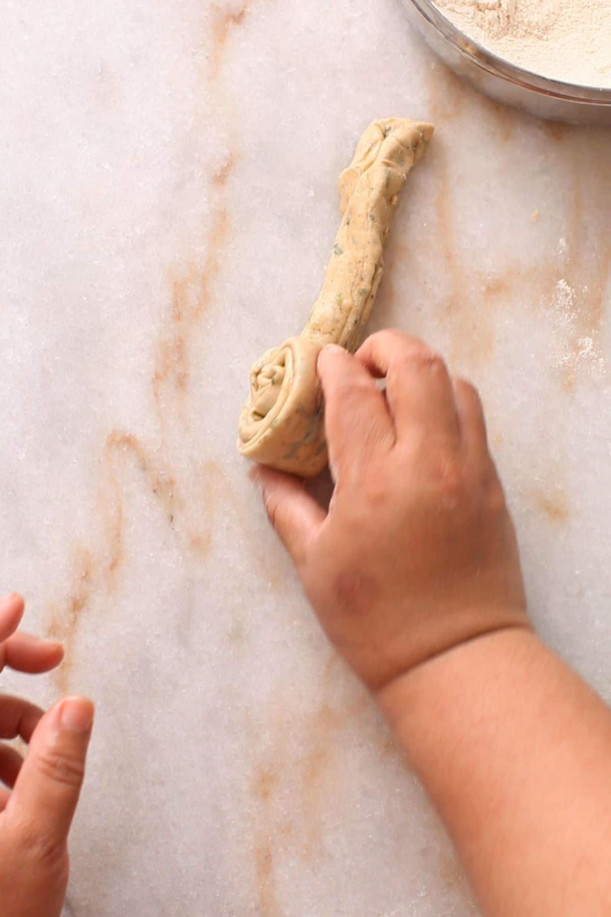 Rolling pleated dough on a marble surface, shaping it into a spiral.