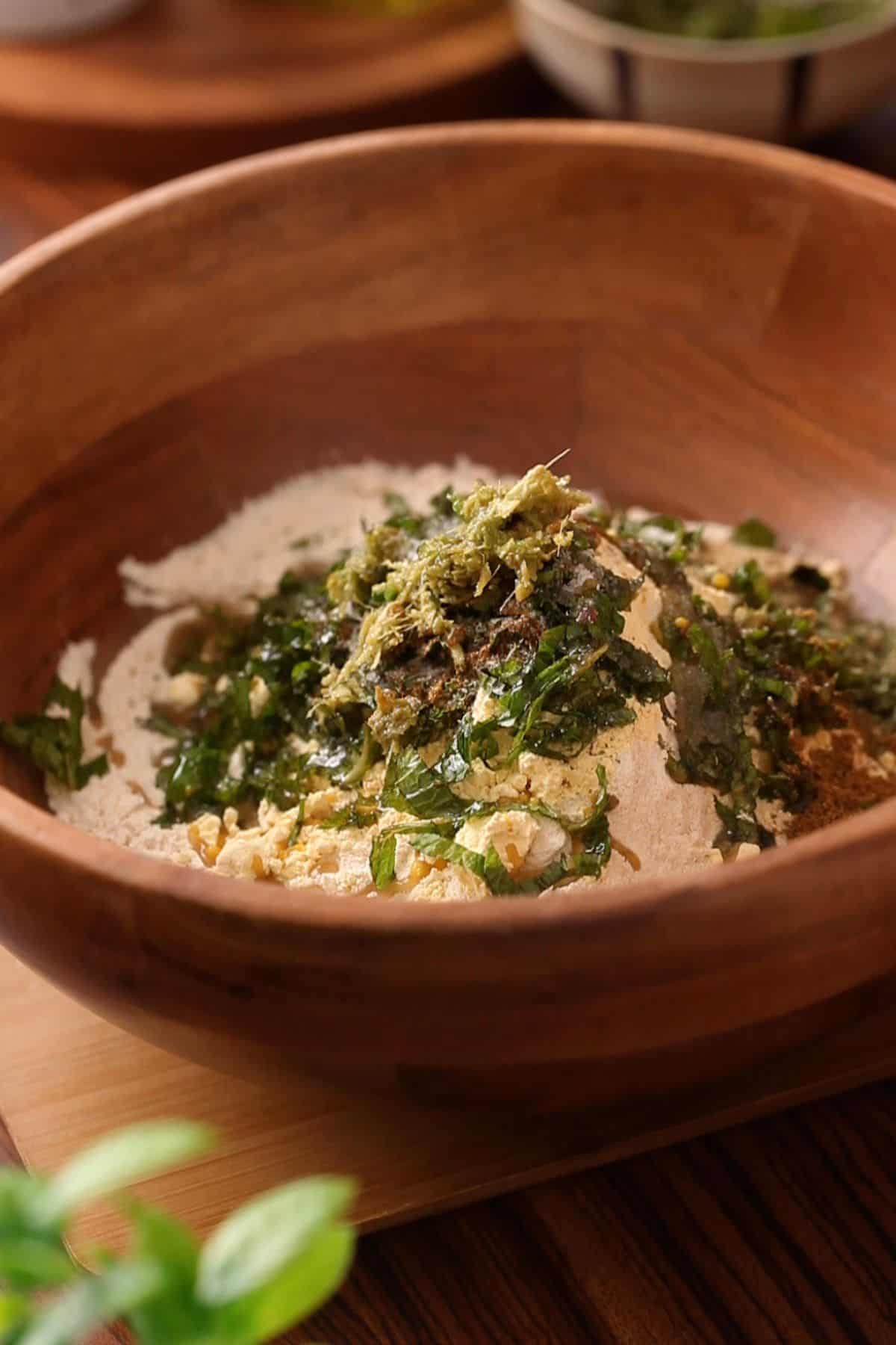 Flour, spices and herbs are added to a large wooden bowl.