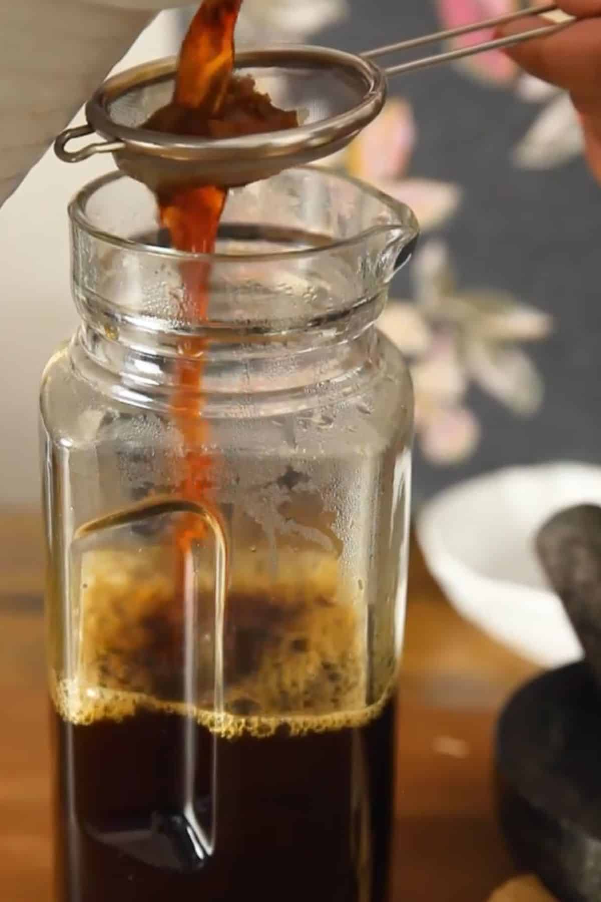 Chai concentrate is being strained into a glass jar.
