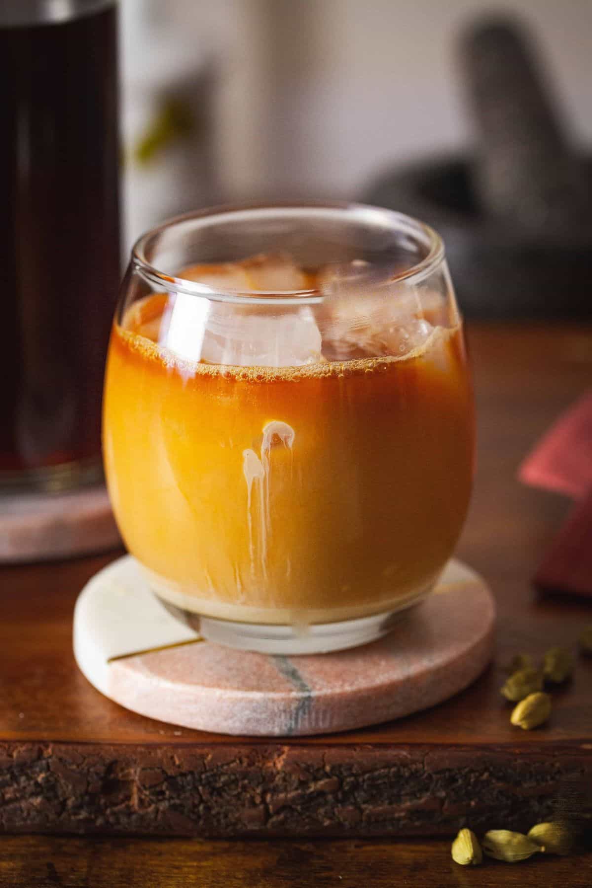 A cup of iced chai placed over a marble coaster with chai concentrate in background.