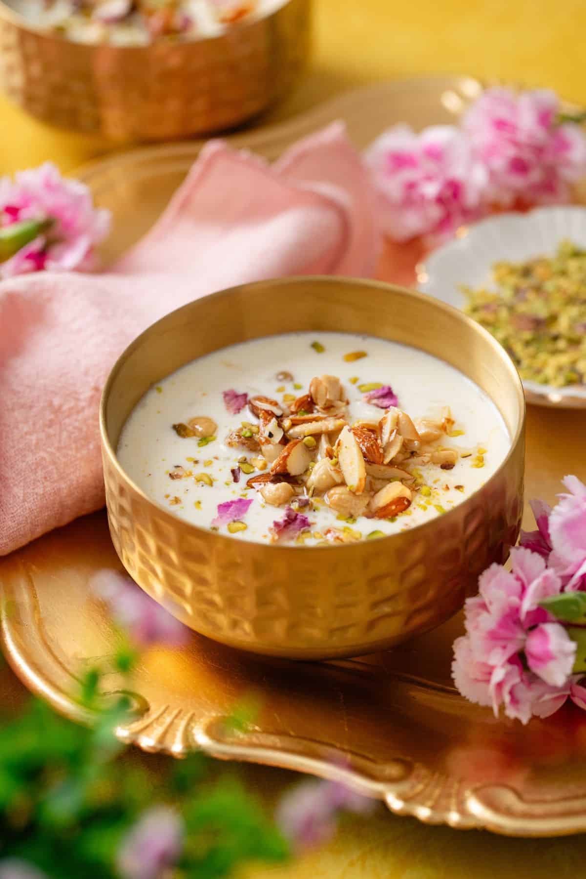 Rice pudding served in a hammered gold bowl with small dish in bacjgroud containing pistachios.