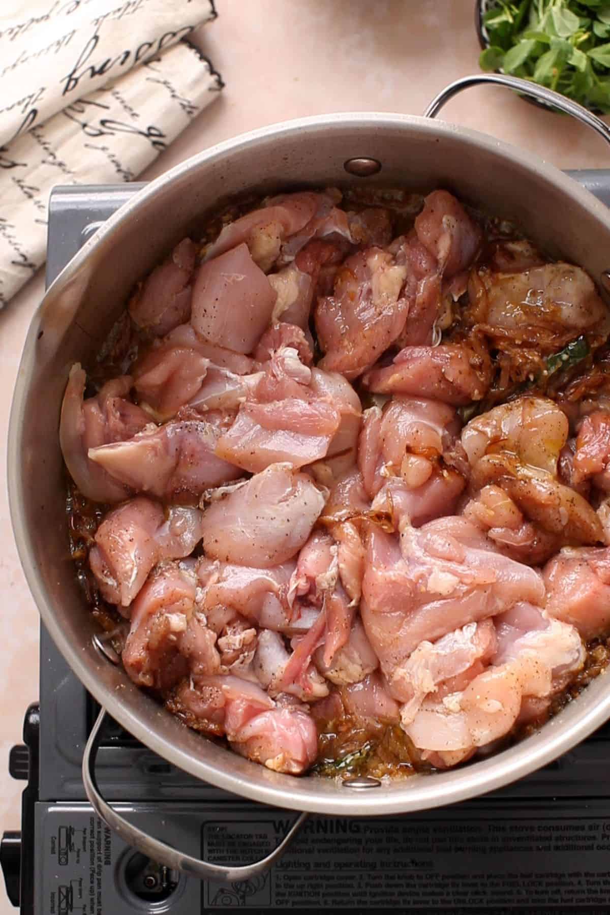 Raw chicken is added to the browned onions.