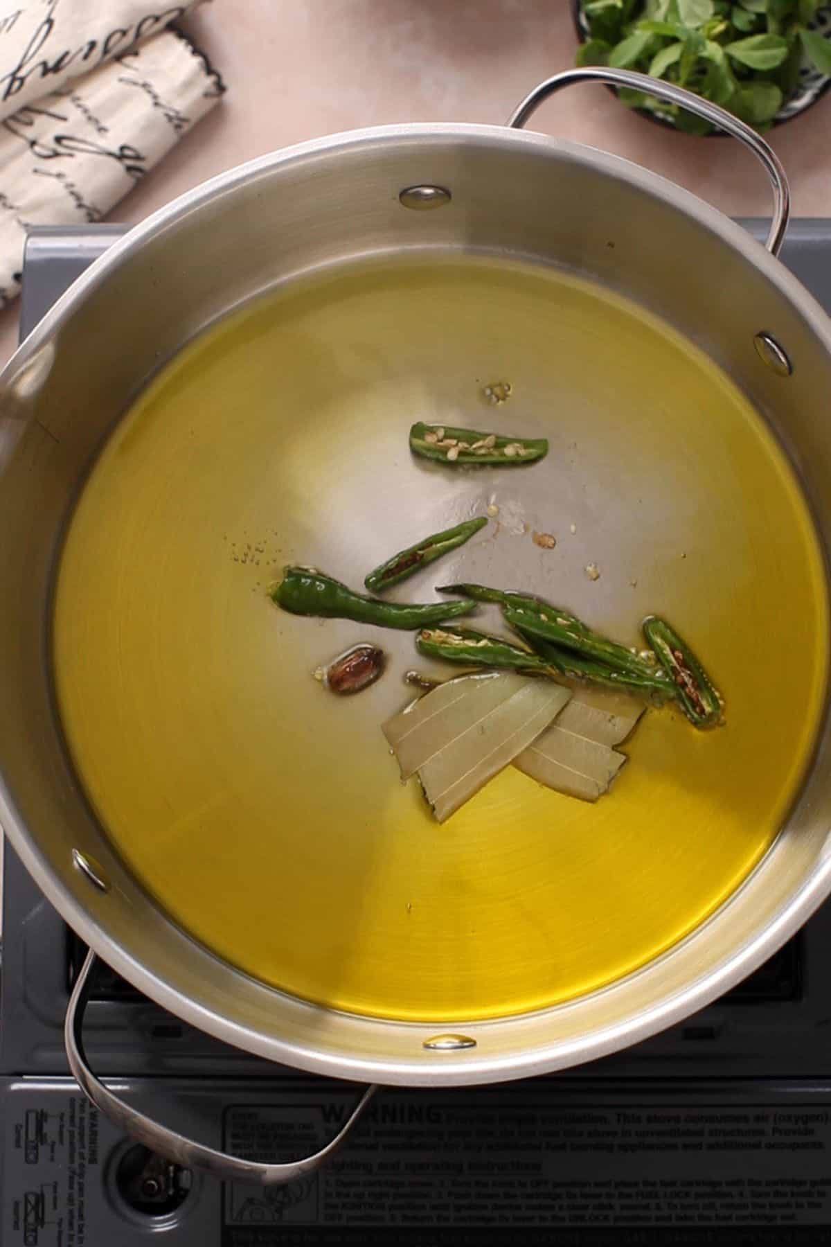 Mustard Oil is tempered with spices and green chillies in a steel cooking pot.