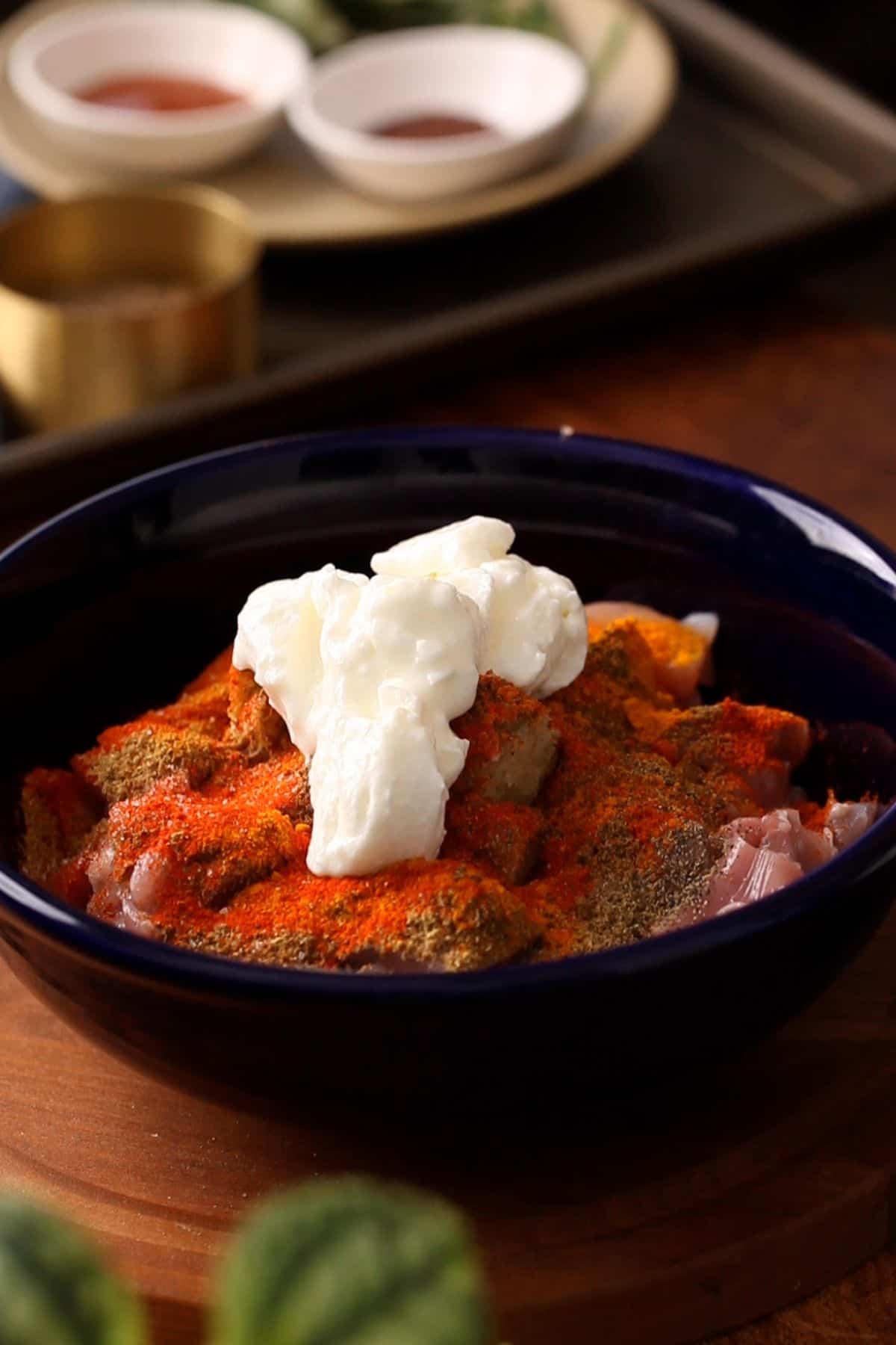 Marinade ingredients are added to the chicken in a black bowl.