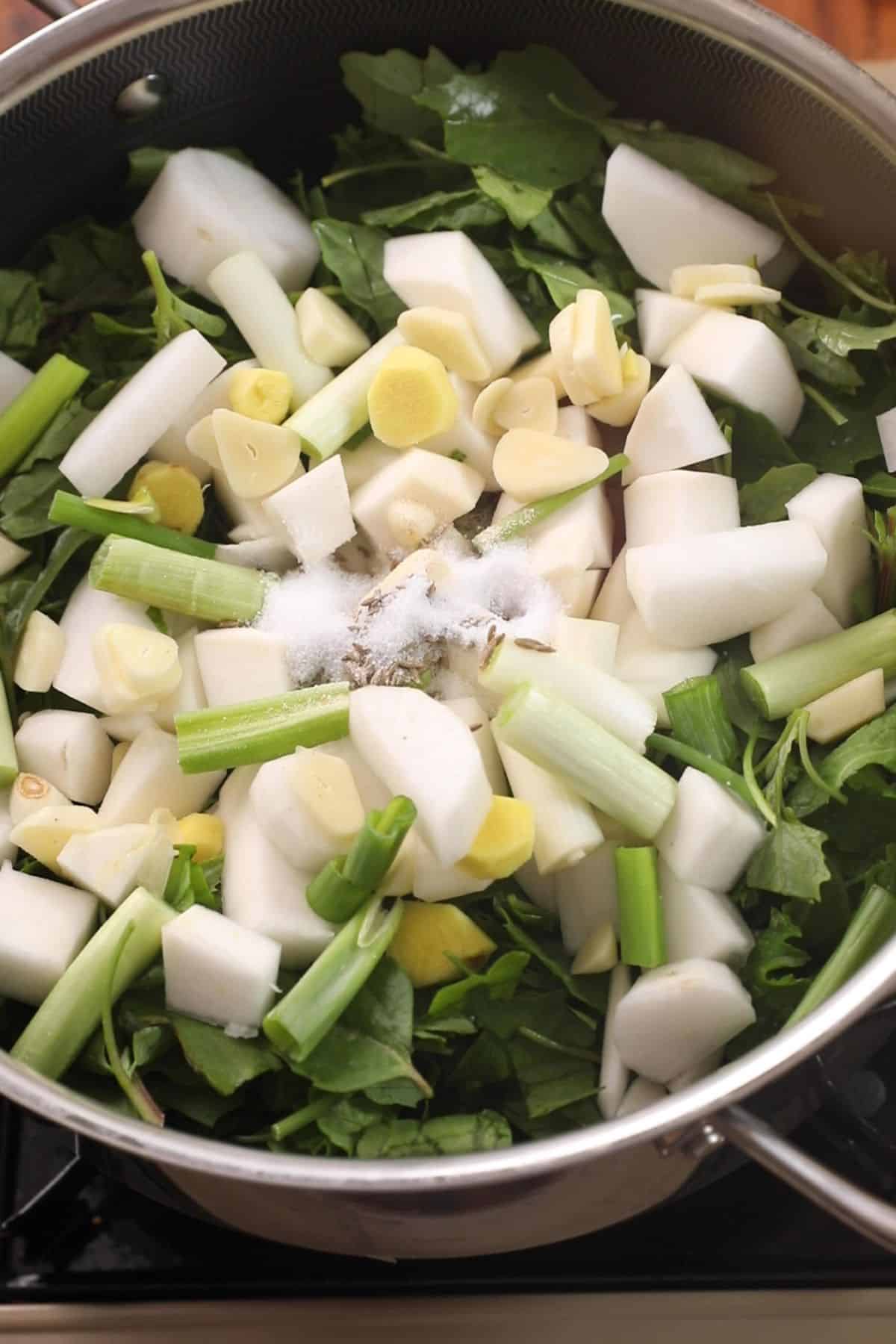 Boiling greens and vegetables on low heat in a large cooking pot.
