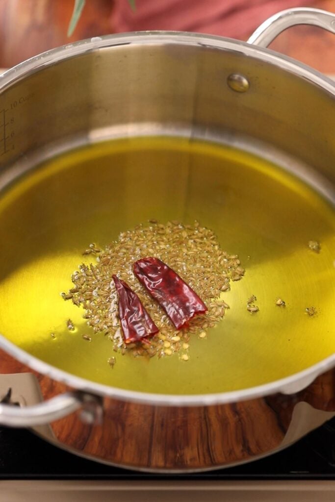 Temper mustard oil in a steel cooking pot with cumin and chillies.