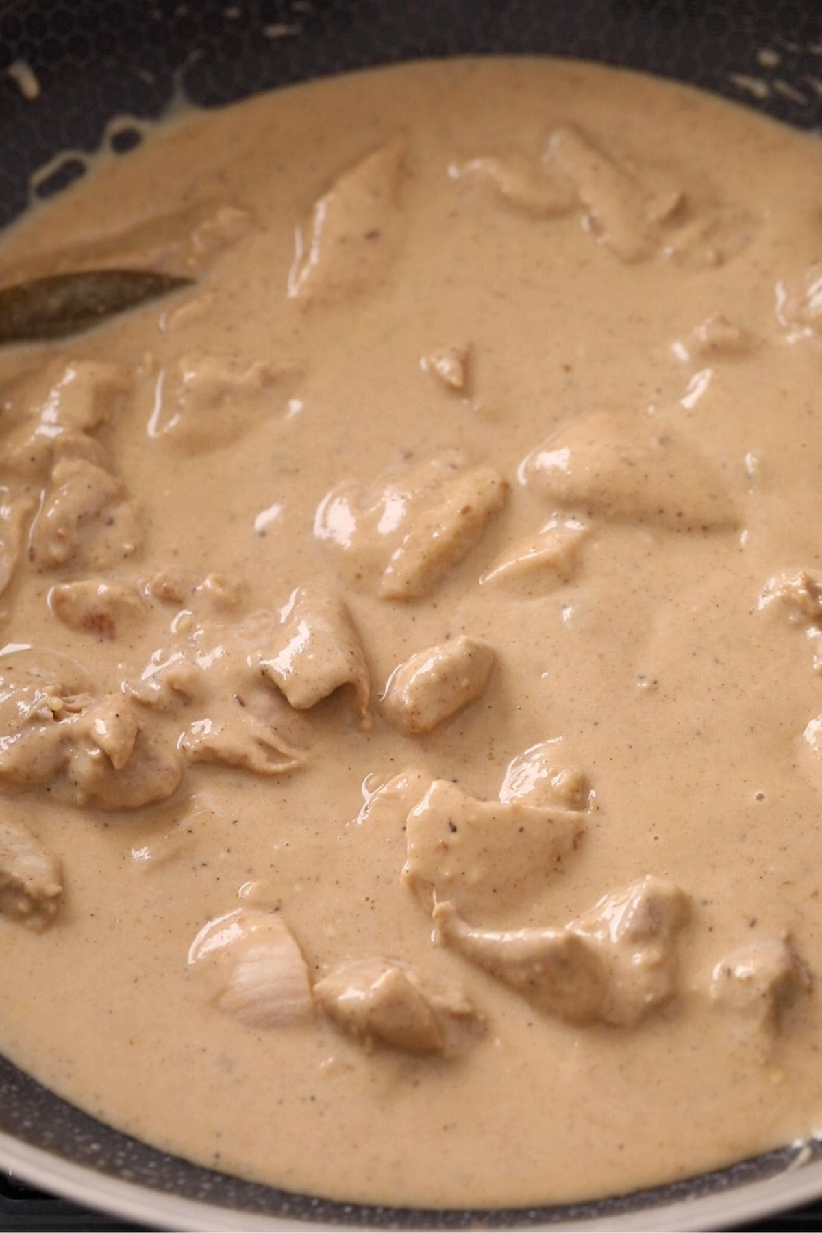 Chunks of chicken simmering in a creamy, beige-colored sauce inside a pan.