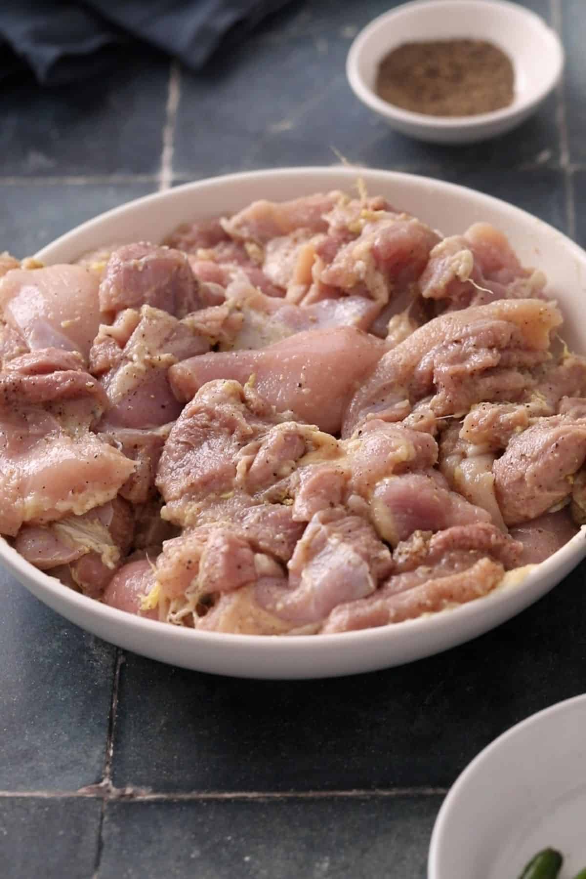 Chicken pieces marinated with black pepper are placed in a shallow white bowl.