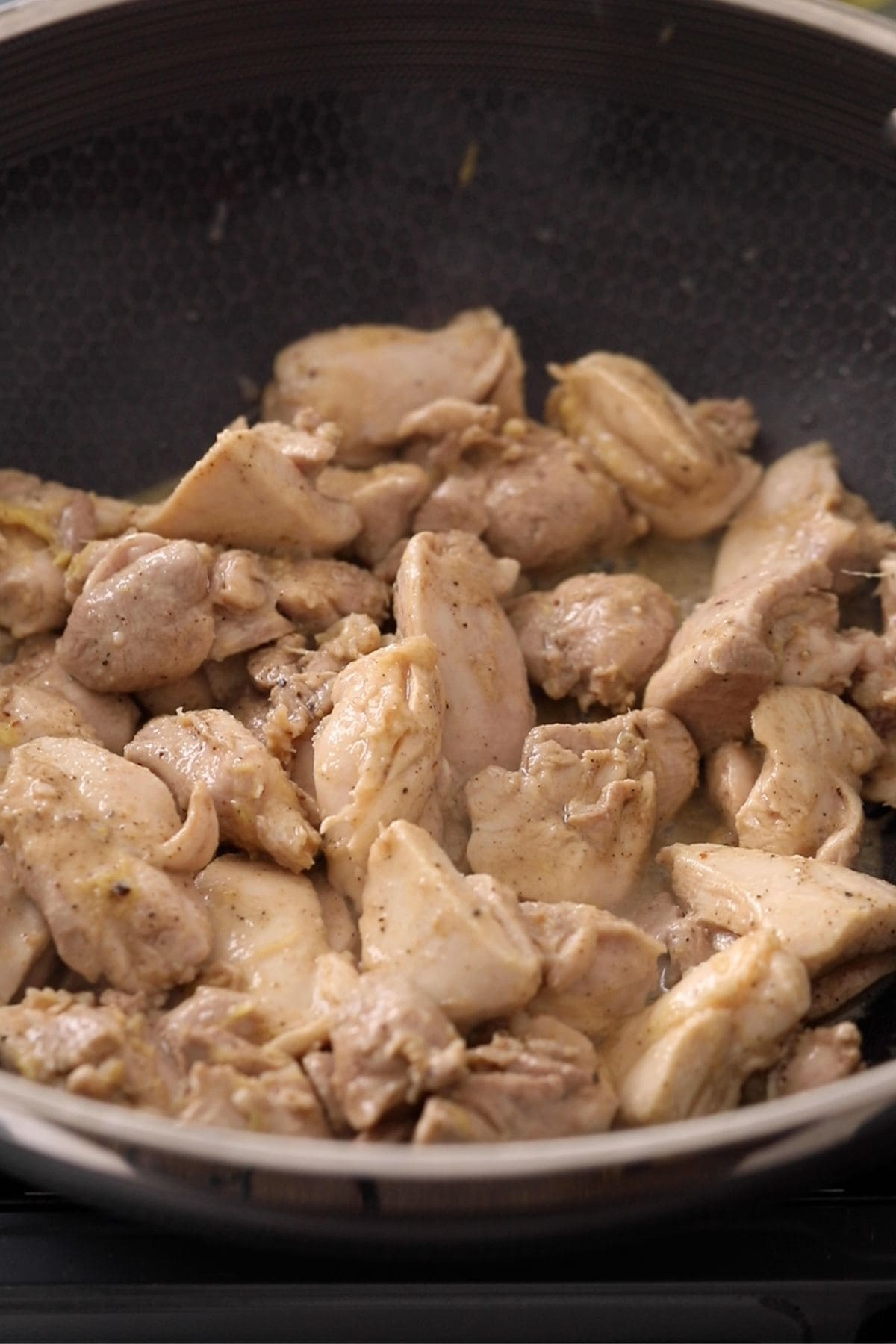 Marinated chicken pieces are cooking in a black, nonstick skillet.
