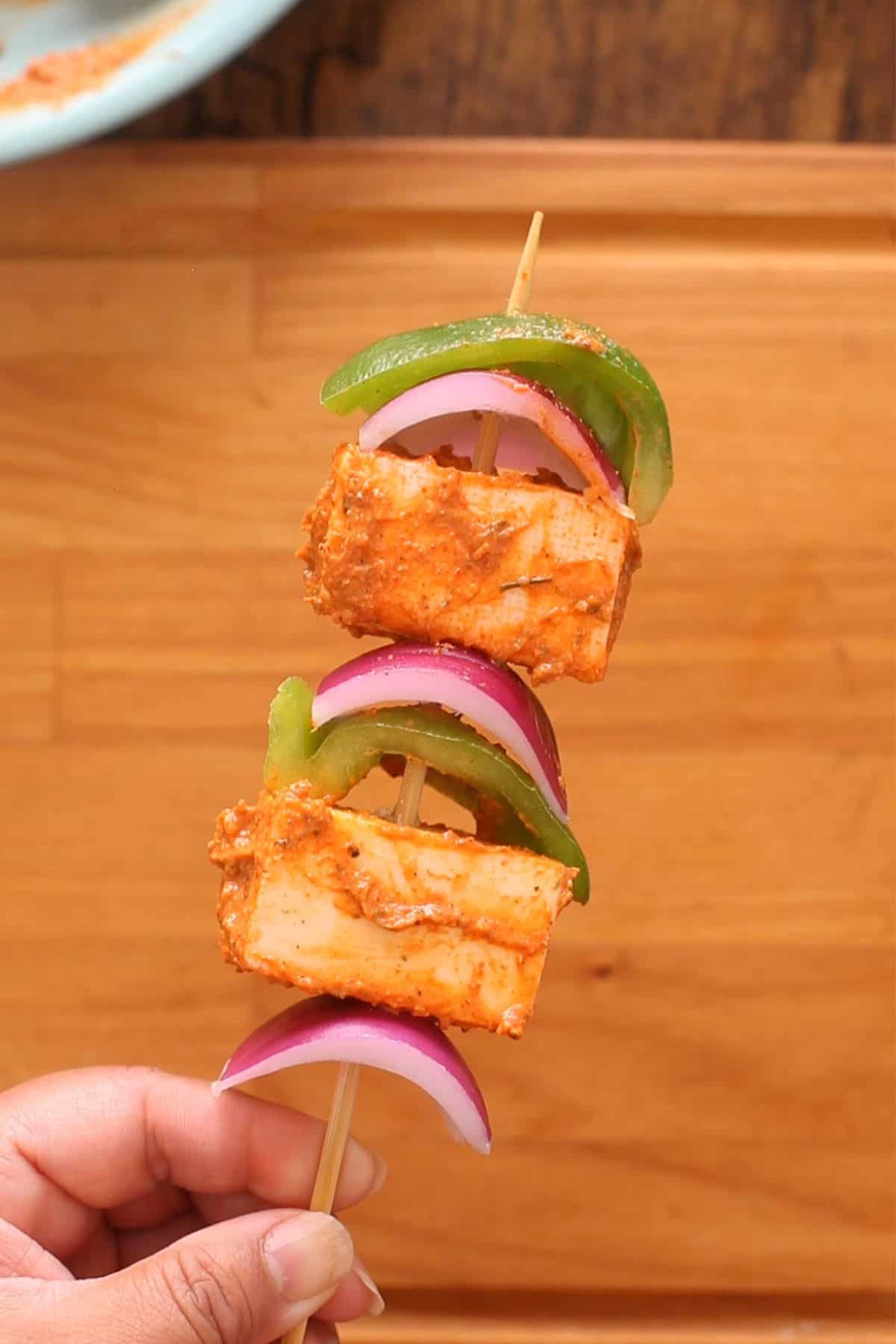Marinated paneer, green pepper and onion pieces are threaded on wooden skewers.