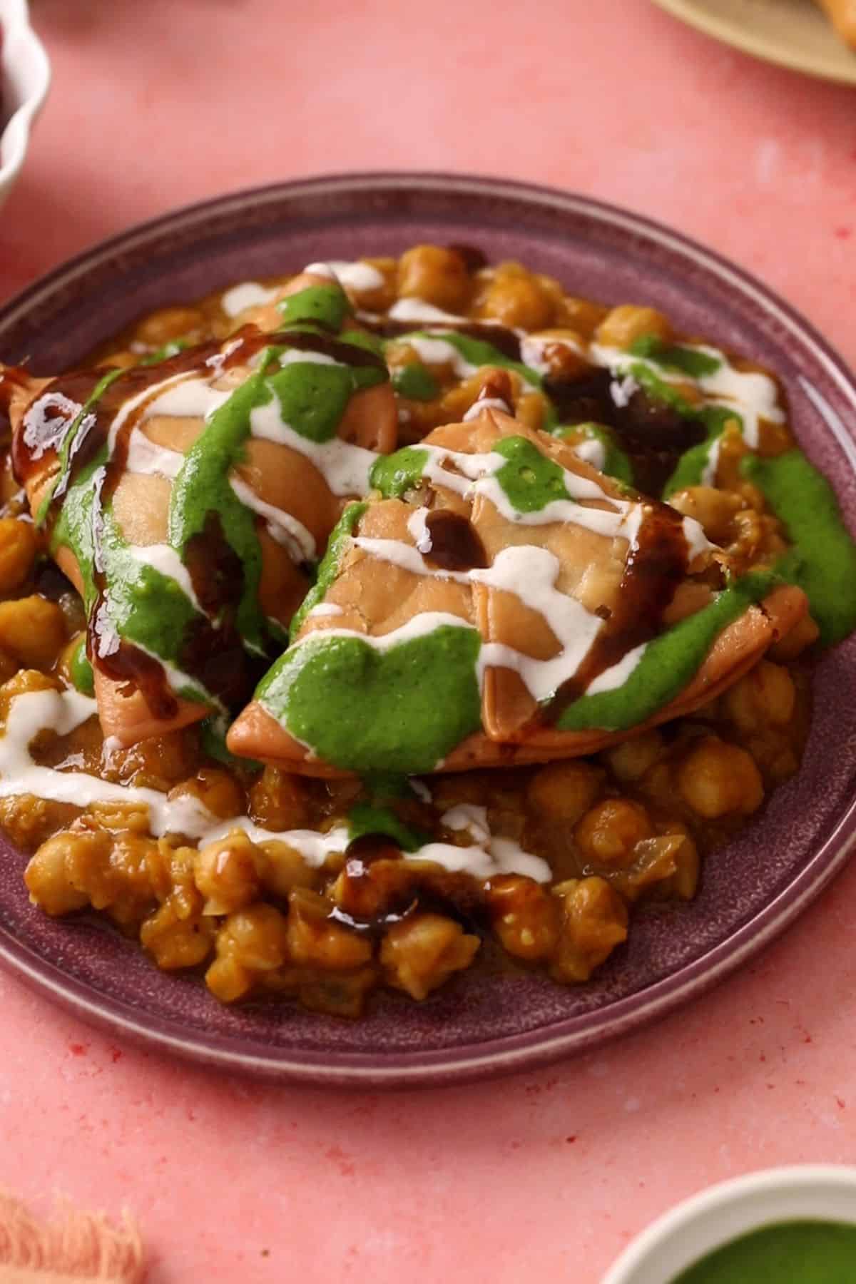 Samosa chana chaat is topped with yogurt and green and sweet tamarind chutneys.