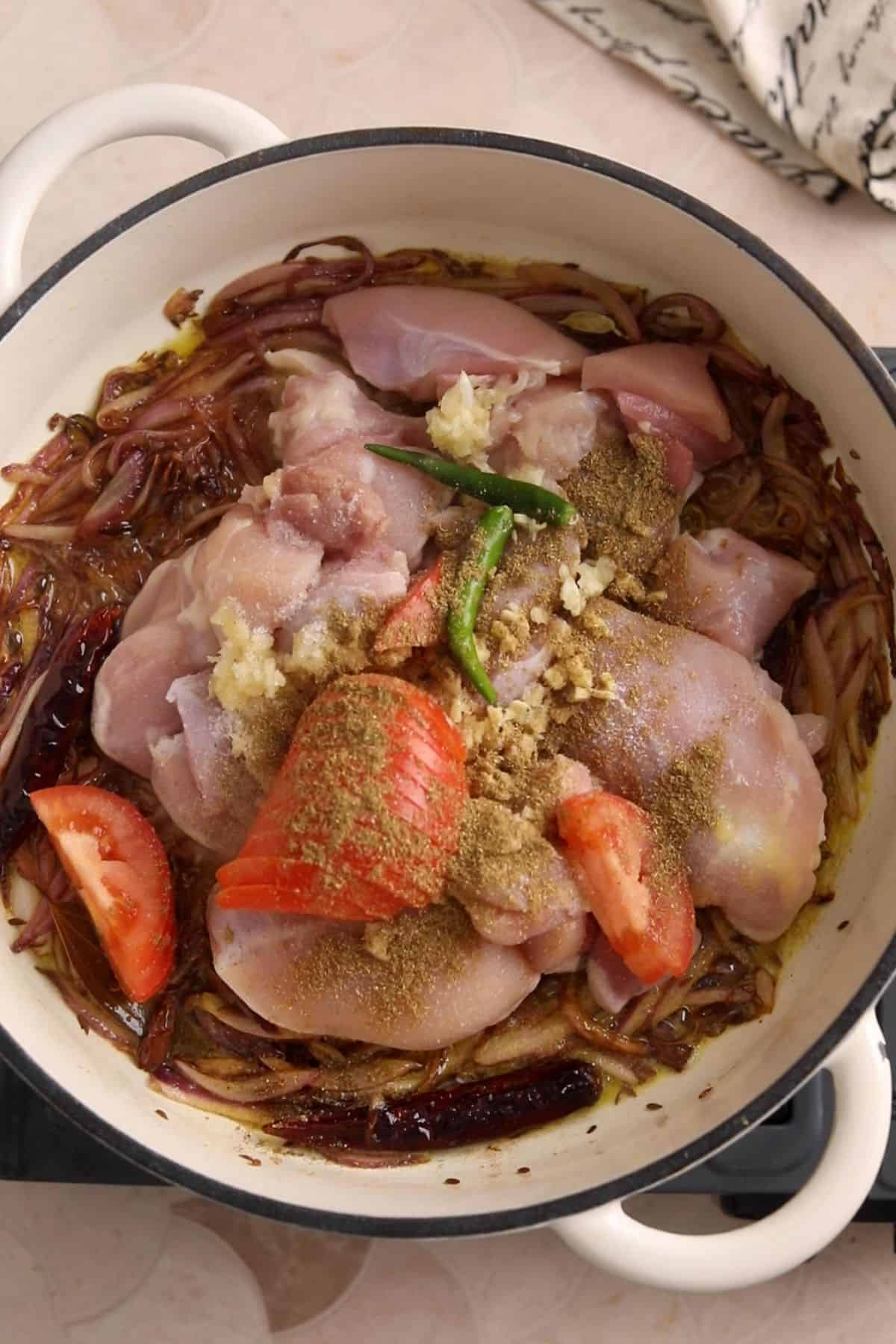 Chicken, tomatoes and spices are added to browned onions