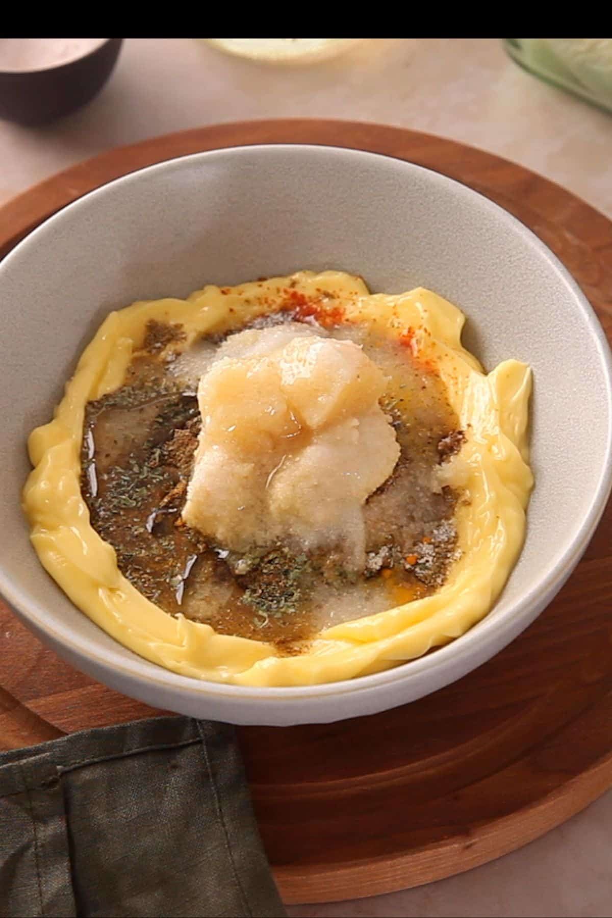 Softened butter mixed with all spices, herbs , ginger and garlic in a grey bowl.