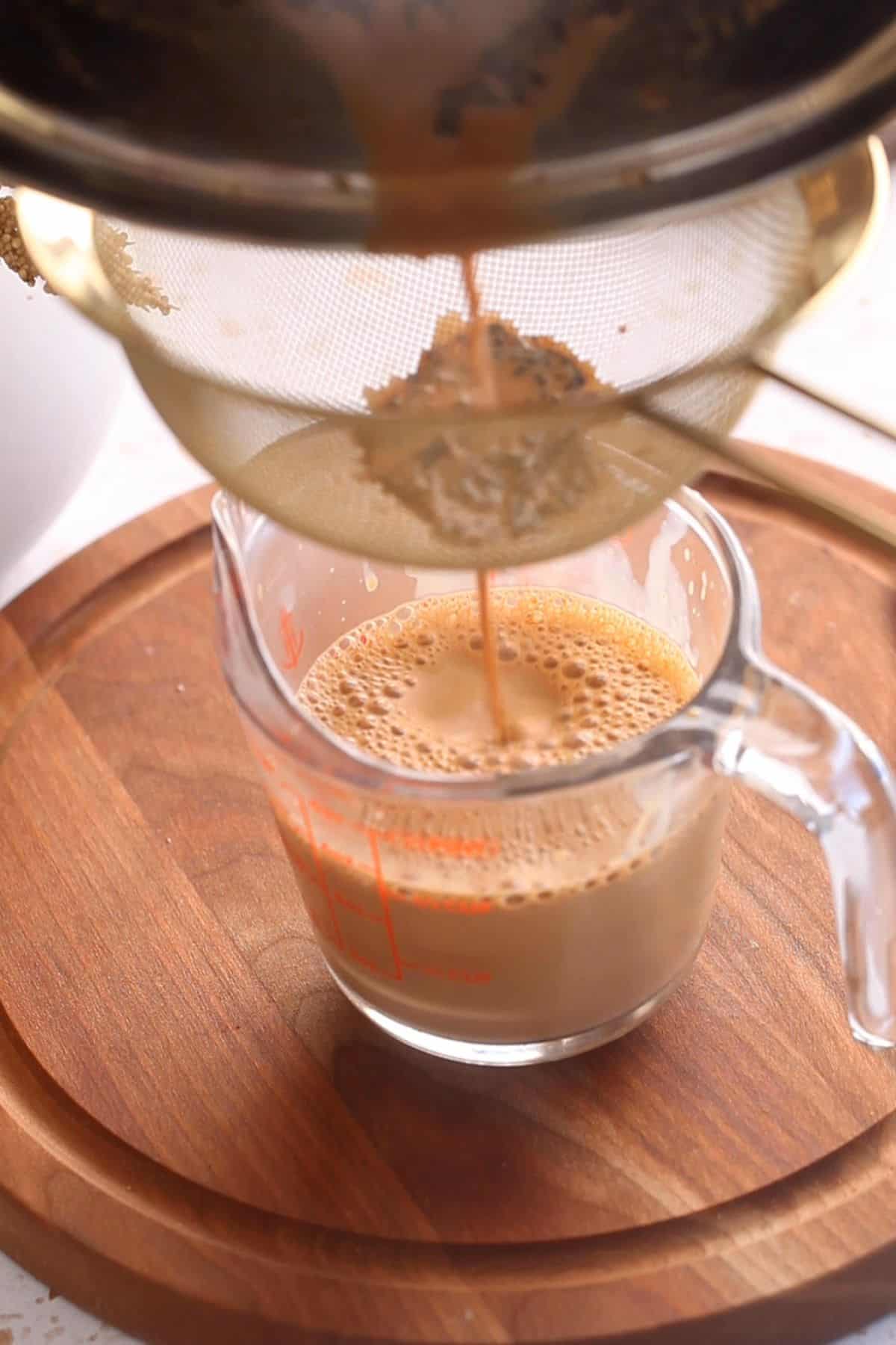 Chai is strained into a measuring cup.