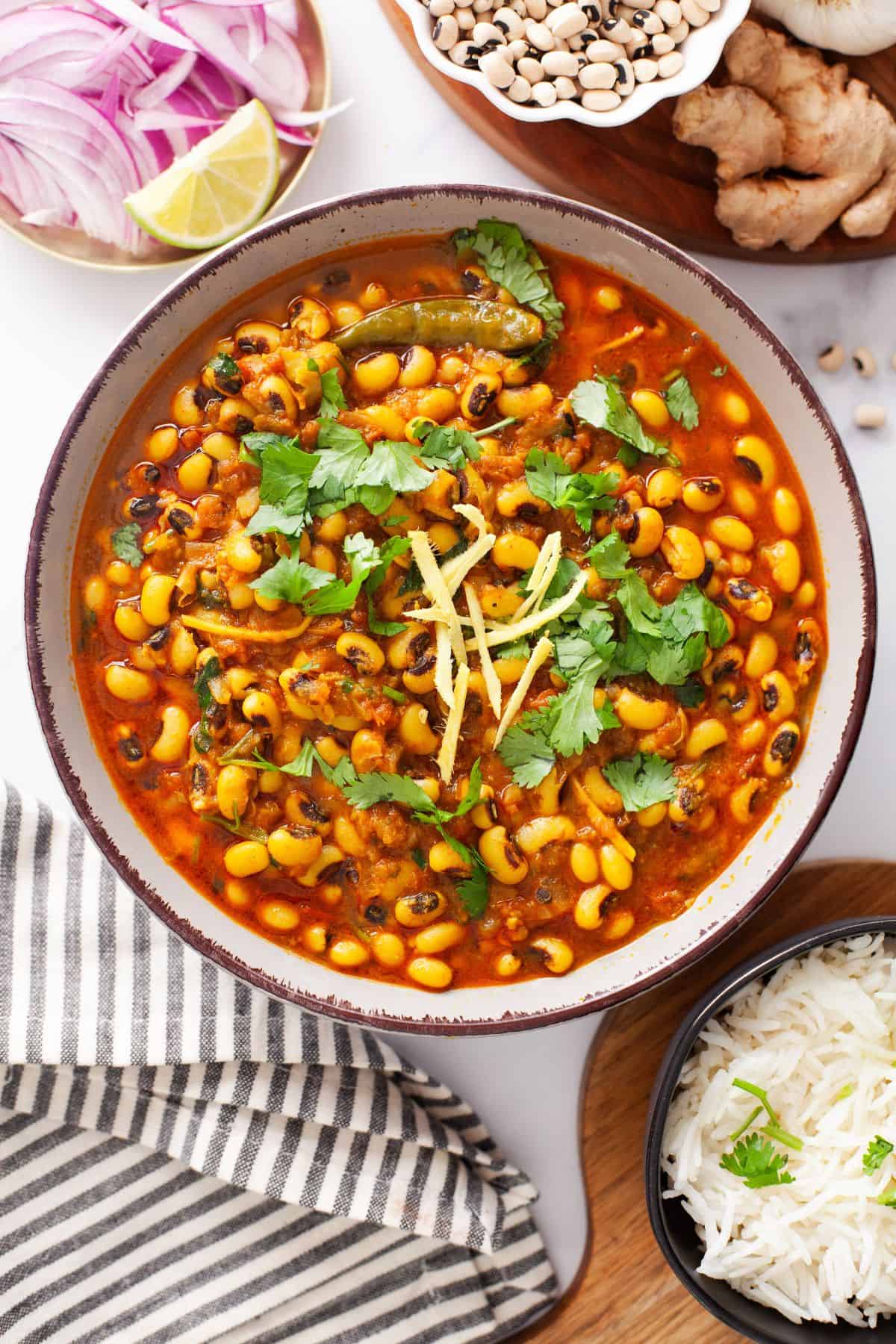 Lobia masala served in a white bowl with rice, onions and lemon.