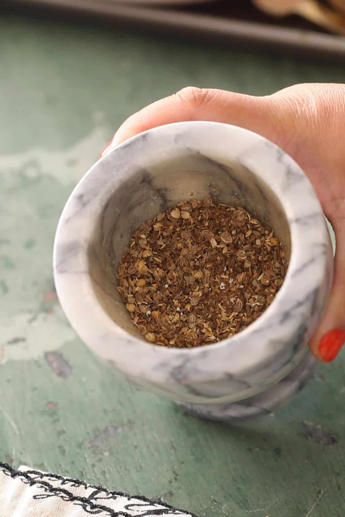 Roasted whole spices are pounded in a mortar pestle to make powder.
