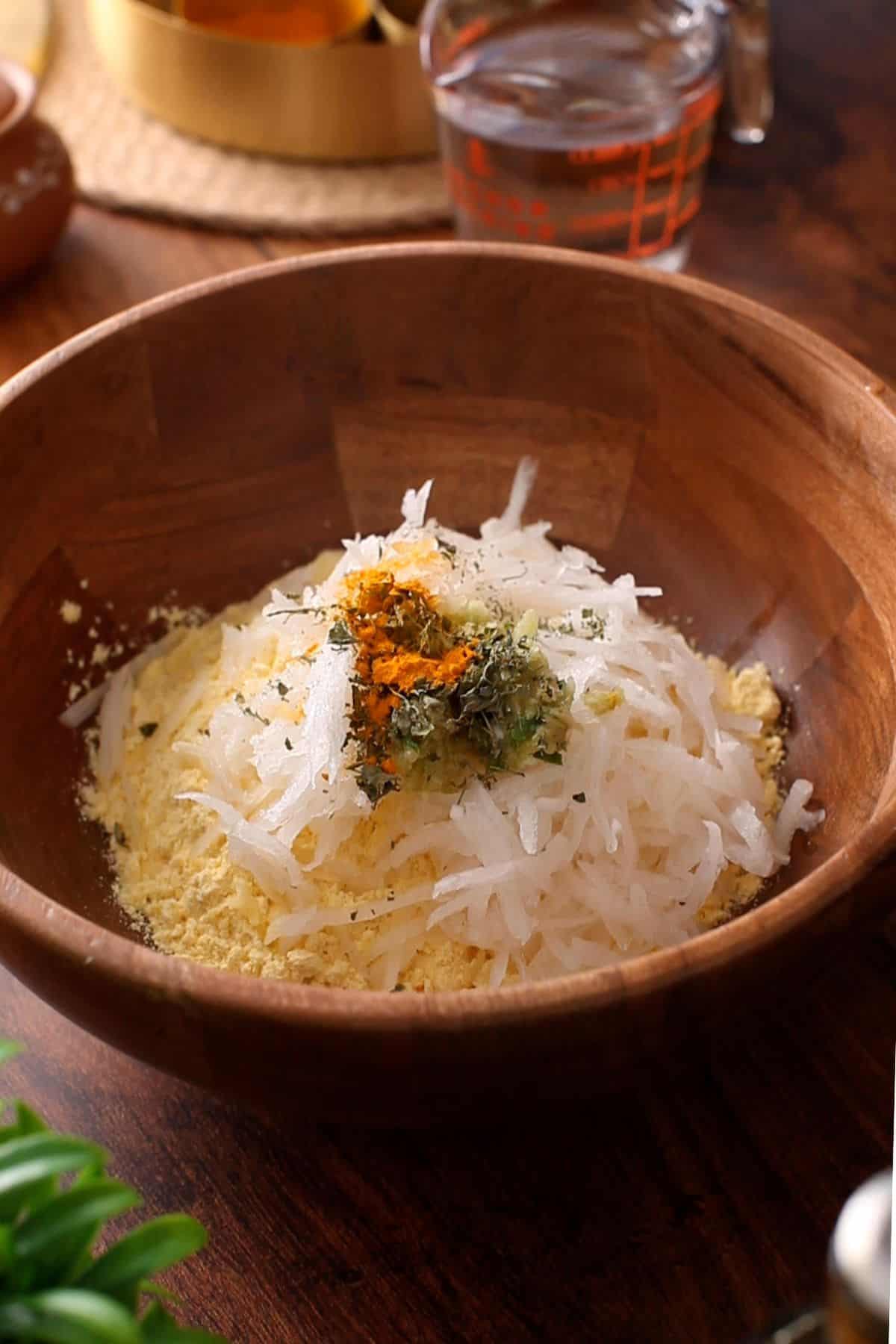 A large brown mixing bowl with cornmeal flour, grated radish, spices and salt.