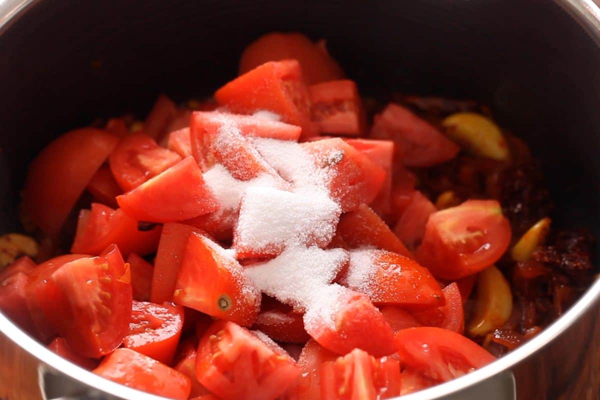 Tomatoes and sugar are added to the cooking pot.