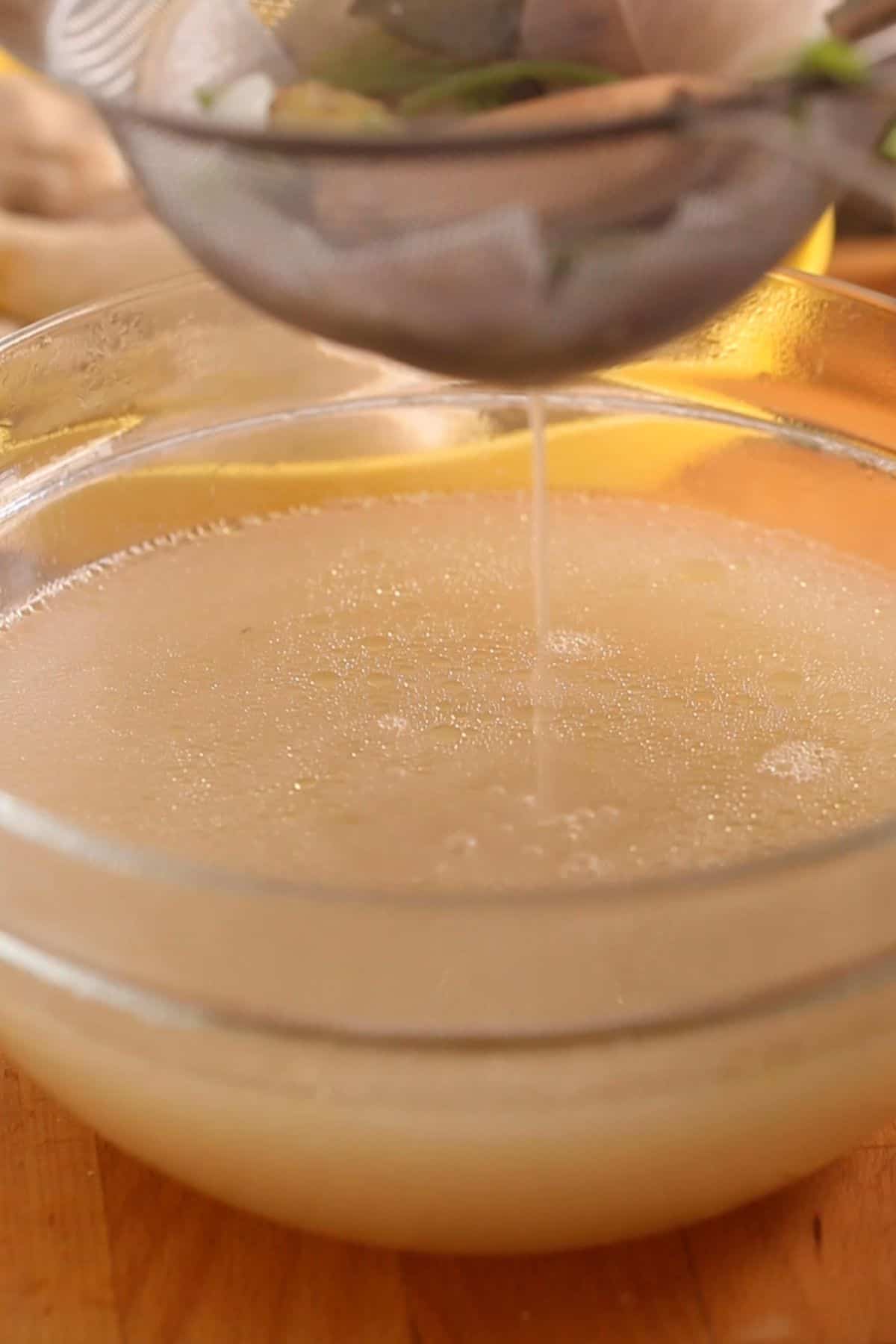 Chicken broth is strained using a stainless steel mesh.