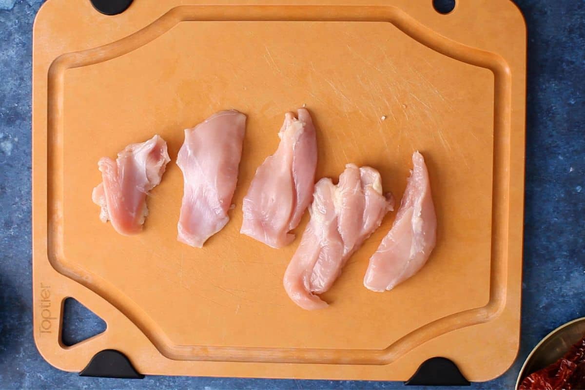 Slices of raw chicken thighs arranged on an orange cutting board.