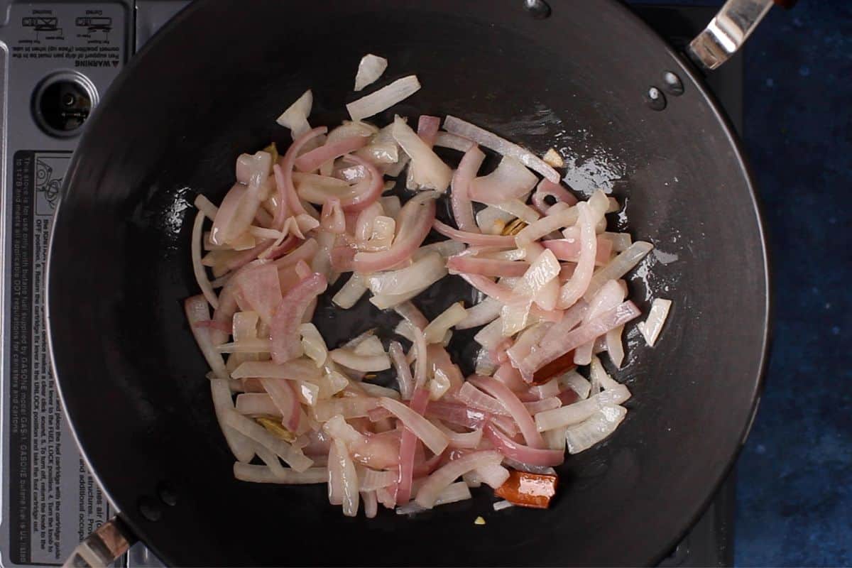 Chopped onions sautéing in a black cooking pot on a stovetop.