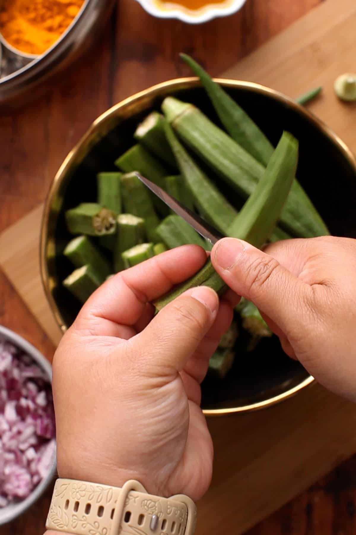 Cutting fresh okra with a small knife over a bowl into halves.